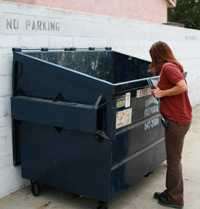 Inspector checking trash bin behind facility