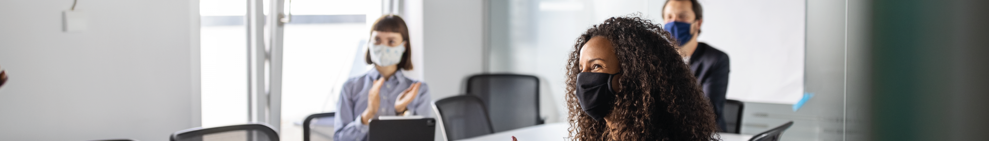 People sitting around a conference table wearing mouth and nose masks