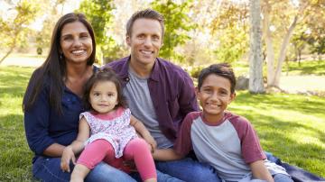 Multi-ethnic family of 4 sitting on grass in park