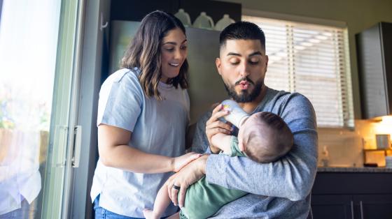 man feeding baby with woman by his side
